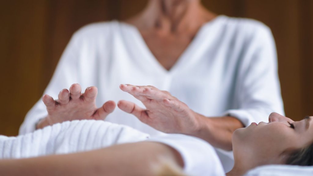 Reiki master providing reiki for stress relief with hands over client during healing session.